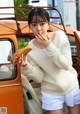 A woman in a white sweater and white shorts eating a sandwich.