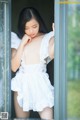 A woman in a white dress leaning against a window.