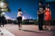 A woman running down a sidewalk at night with a man and a woman in the background.