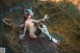 A naked woman sitting on top of a rock next to a dragon.