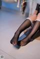 A woman wearing black fishnet stockings sitting on a wooden floor.