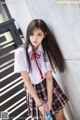 A woman in a school uniform leaning against a wall.