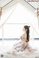 A woman sitting on top of a bed next to a window.