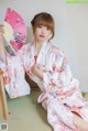 A woman in a kimono sitting on the floor holding a fan.