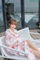 A woman sitting on a white chair on a wooden deck.