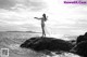 A woman standing on a rock by the ocean.