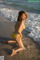 A woman in a yellow bikini sitting on the beach.