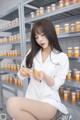 A woman sitting on a stool in front of a shelf of pills.