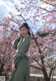 A woman in a green dress standing in front of a tree.