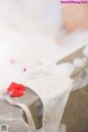 A bathtub filled with white foam and a red rose.