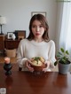 A woman sitting at a table holding a bowl of food.