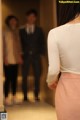 A woman in a white shirt and pink skirt standing in a hallway.