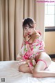 A woman in a pink kimono sitting on a bed.