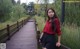 A woman in a red shirt and black shorts standing on a wooden bridge.