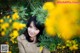 A woman standing in front of a bush of yellow flowers.