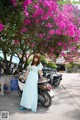 A woman in a blue dress standing next to a motorcycle.