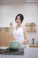 A woman in a white dress holding a spoon in a kitchen.