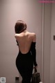 A woman in a black dress standing in an elevator.