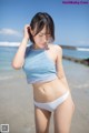 A woman in a blue top and white bikini standing on a beach.