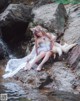 A woman in a white dress sitting on a rock next to a stream.