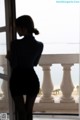 A woman standing in front of a window looking out at the ocean.