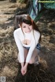 A woman in a white shirt and denim shorts crouching on the ground.